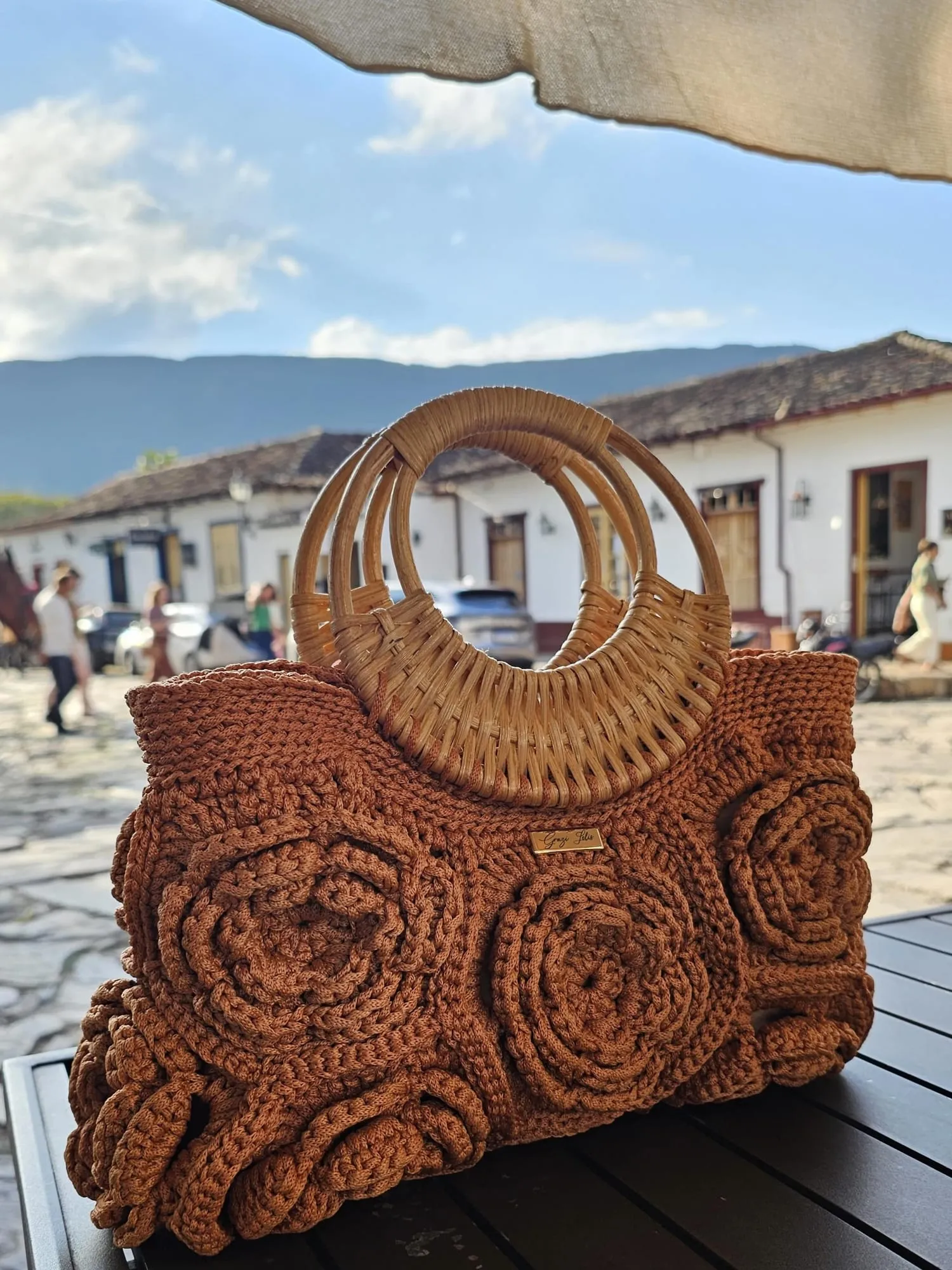 Bolsa Floral Elegância sobre uma mesa numa rua de cidade histórica