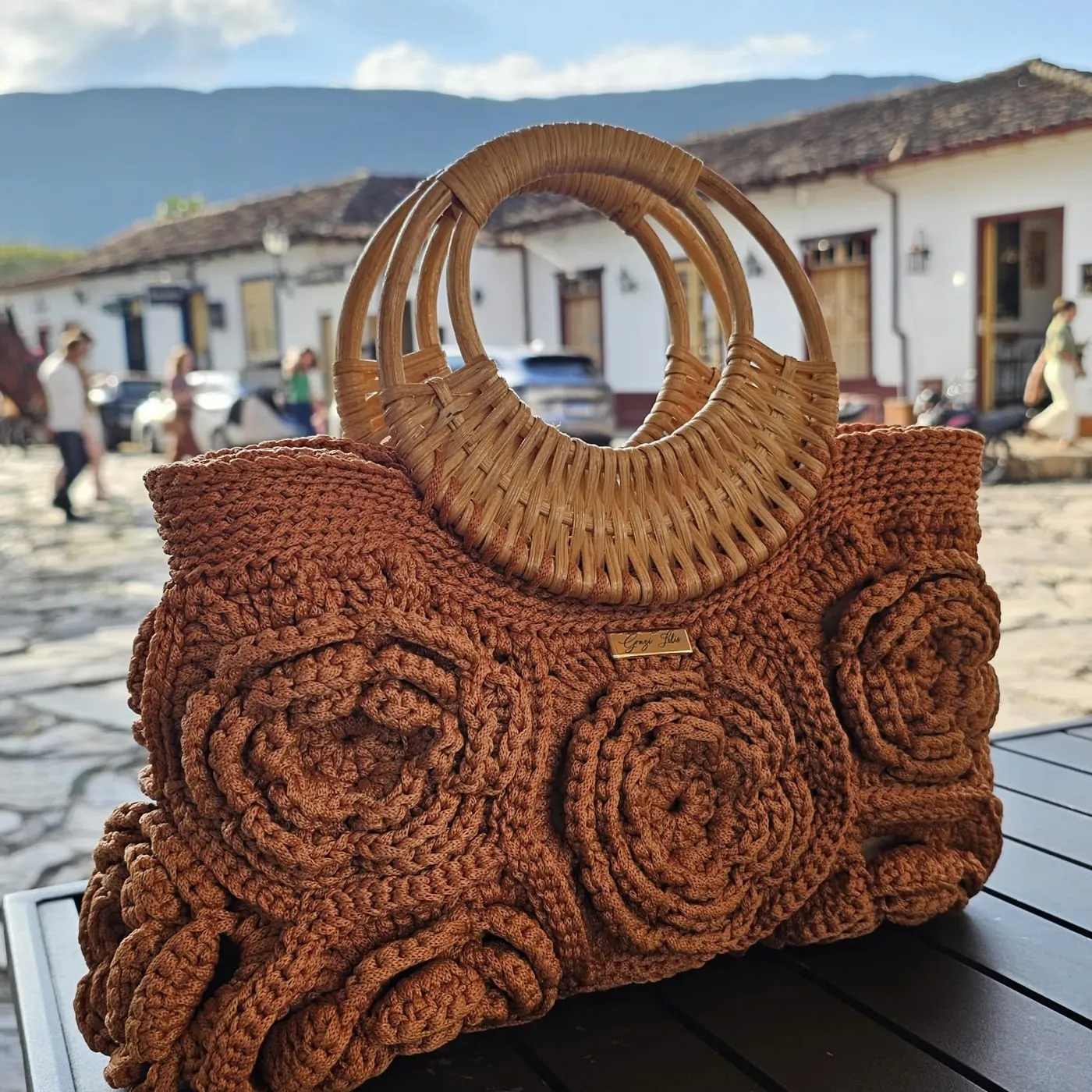 Caramel Elegância Floral Bag with rattan handles in a historic town street